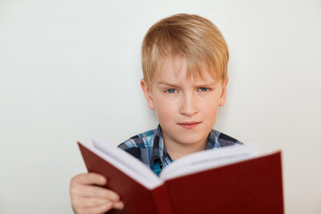 Human face expressions and emotions. Children and education. A close-up of attractive little boy with fair hair reading a book being tired of homework having angry expression. Boring school studies