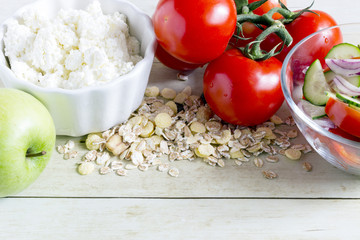 Foods for healthy eating: cottage chesse, tomatoes, apple, cereal, salad on light wood background