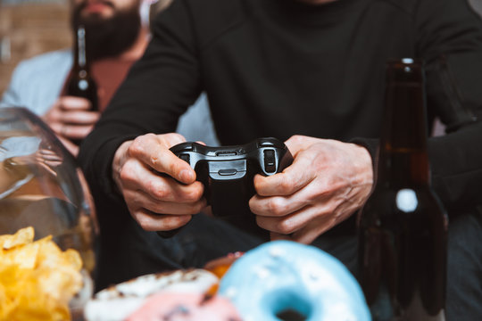 Close up men at home with a beer and chips with joysticks in hand playing computer video game. The concept of friendship, technology and weekend