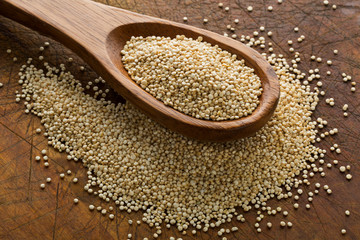 Raw, whole, unprocessed quinoa seed in wooden spoon on wood board