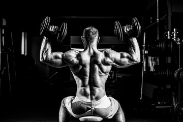 Muscular man training his shoulders with dumbbells in gym