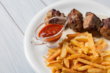 Grilled shish kebab served with french fries and sauce on wooden table. Close up with selective focus