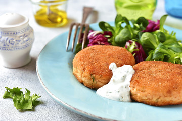 Salmon patties with mix salad leaves and yogurt sauce.Top view.