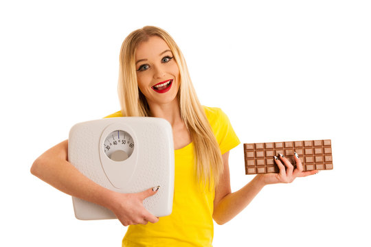 Undecided woman holding scale and chocolate uncertain wether to loose weight isolated over white background