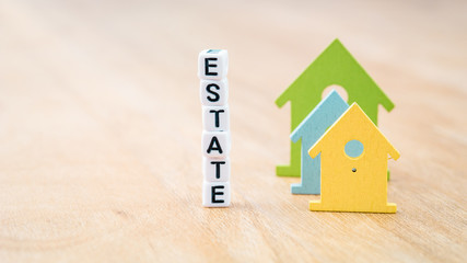 ESTATE word of cube letters behind coloured house symbols on wooden surface. Concept