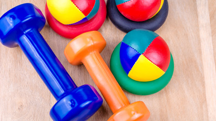 Blue and orange dumbbells and coloured balls on wooden surface