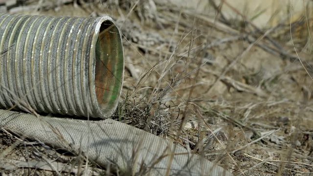 An abandoned piece of lay-flat water hose and green plastic ribbed suction hose used in the mining industry rotting away in the environment and contributing to environmental pollution and waste.