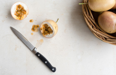 High angle view of panama gold passionfruit in halves with knife and basket on cream limestone background
