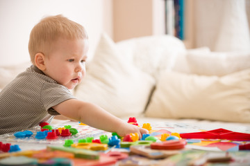 Cute preschooler child boy plays with mosaic at home. A blond little toddler playing in kid's room. Leisure activities. indoors. Boy sorting colorful children's plastic mosaic. Development.