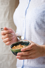 Young woman with muesli bowl. Girl eating breakfast cereals with nuts, pumpkin seeds, oats and yogurt in bowl. Girl holding homemade granola. Healthy snack or breakfast in the morning.