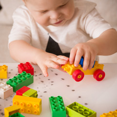 Close up of child's hands playing with colorful plastic bricks at the table. Toddler having fun and building out of bright constructor bricks. Early learning.  stripe background. Developing toys