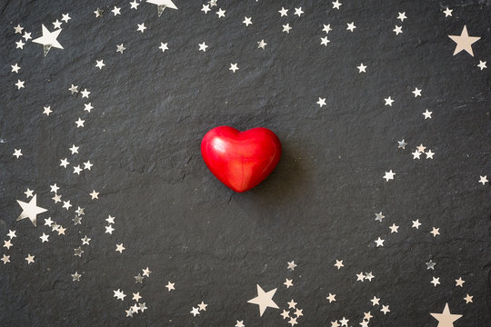 Small red heart on the black background with silver stars. Hearts and stars on a black board. Background. Valentine's and Christmas.