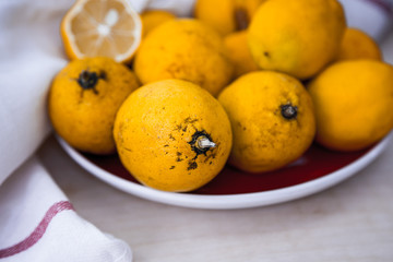 Fresh lemons on the red plate. Cut and full. White fabric.