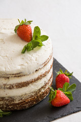 Delicious white cream icing cake with strawberry on the black board. Naked cake with cream, decorated with strawberries and mint.