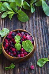 Frozen berries, red and black currants, blueberries and raspberries with fresh mint leaves in wooden bowl