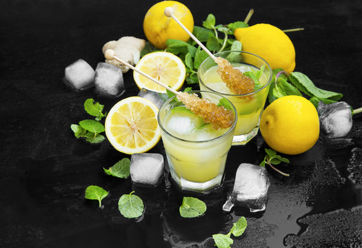 Fresh mojitos cocktails with lemons, fresh mint, ice cubes and sugar sticks on wooden background
