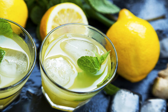 Fresh mojitos cocktails with lemons, fresh mint, ice cubes and sugar sticks on wooden background