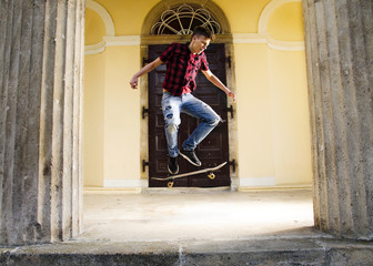 Teenage skater jumps in air with skateboard, rustic house in background 