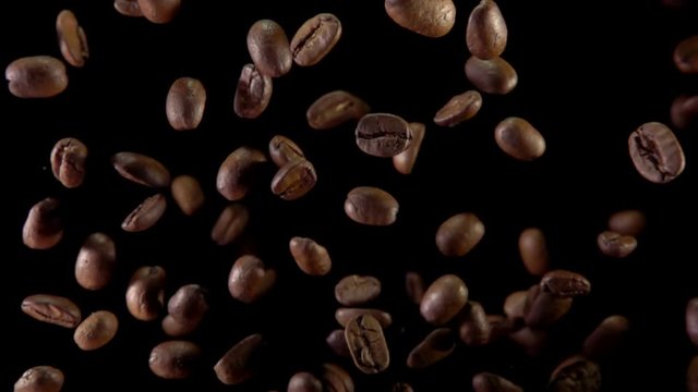 Fried coffee beans fly to the camera on a dark background. Slow motion