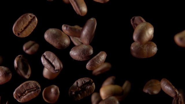 Fried coffee beans fly to the camera on a dark background. Slow-motion shooting, very close-up