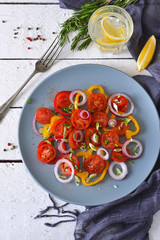 Salad with tomatoes, pepper and red onion with sauce on a gray plate on a white background.