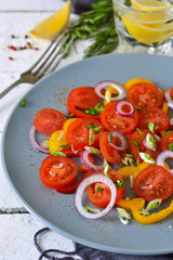 Salad with tomatoes, pepper and red onion with sauce on a gray plate on a white background.