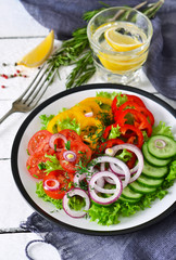 Vegetable mix salad with avocado and olive oil sauce on a white, wooden background.
