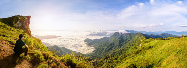 Panorama beautiful landscape nature, Male tourist are watching sunrise on peak mountain with sun cloud fog and bright sky in winter at Phu Chi Fa Forest Park, famous attraction of Chiang Rai, Thailand