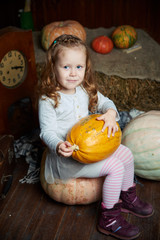 Fototapeta premium Portrait of adorable smiling girl posing with orange pumpkin in fall wooden interior. fine