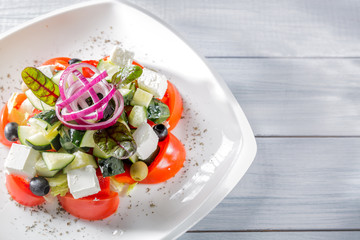 Fresh Greek salad on white plate with onion. Close up with selective focus