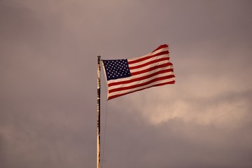 A weathered American Flag waving under a cloudy sky.