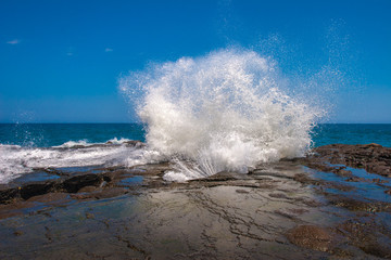 The wave breaks over the rocks.