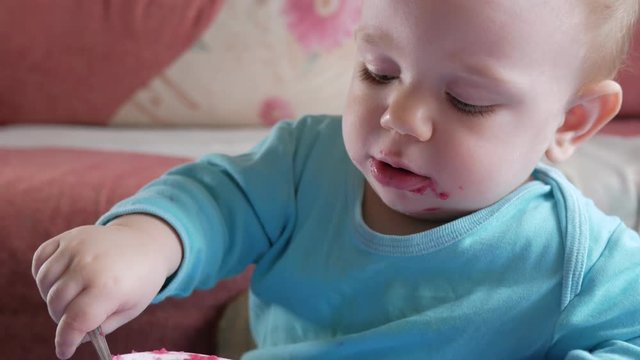 An attractive boy 2 years old eats a red beet salad. The face is smeared with porridge. Sits on the table.