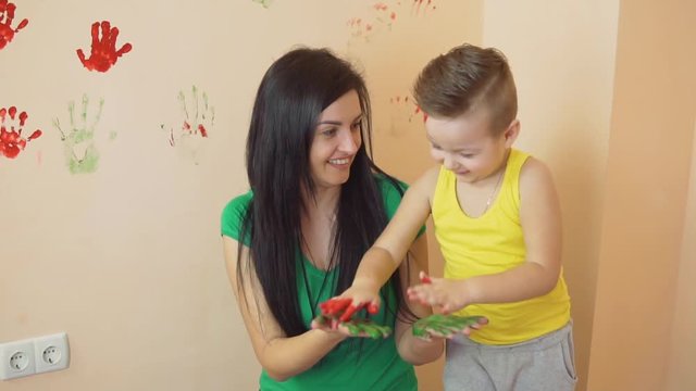 Young mother with her little boy are lmixing colors at their hands yo leave beautiful handprints on the wall. Mother and child concept. Slowmotion.