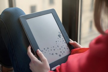 A woman sits by the window and uses an e-book. blank screen