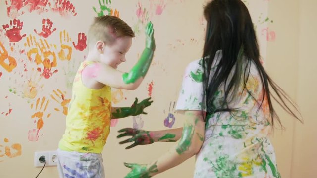 Young mother with her little boy are lmixing colors at their hands yo leave beautiful handprints on the wall. Their clothes are dirty in color. Mother and child concept. Slowmotion.
