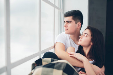 A loving couple are lying by a window bathed in sunlight. Bright and cozy bedroom. Family comfort and love