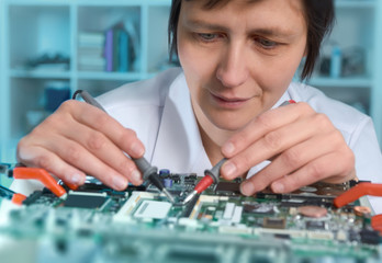 Middle-aged caucasian female engineer or tech repairs faulty motherboard