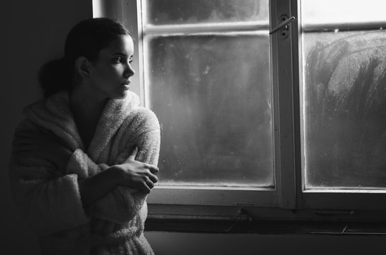 Beautiful ill sad cancer patient girl in pajamas  looking through hospital window in black and white