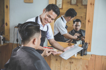 barber showing tablet to his client while sitting on barbershop