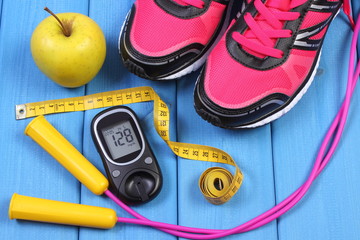 Glucometer, sport shoes, fresh apple and accessories for fitness on blue boards