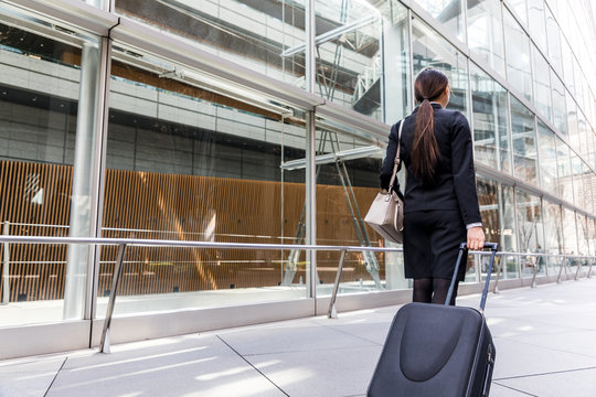 business woman walking by pulling a suitcase near a building