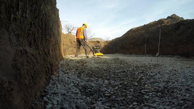 The man at the construction site.
Man serving compacting machine. Stone compaction during the construction of a private swimming pool.

