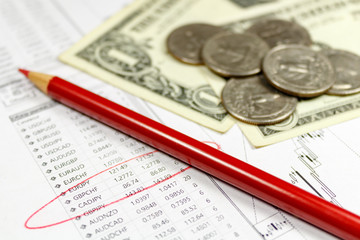 Coins with US dollars banknotes and red pencil on the background of table of exchange rates. Focus in the text