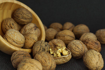 Walnuts are scattered from a bamboo bowl on a black background, one is uncovered