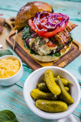 Tasty burger with beef with spinach and gherkin served on a small board on a wooden background.