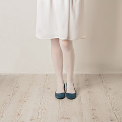 Female legs in white tights, skirt and ballet flats on a white background.