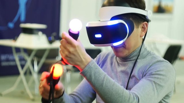 A young man uses VR-headset display and headphones for virtual reality game