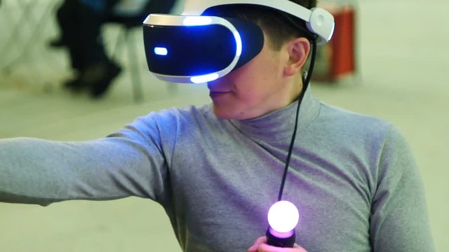 A young man uses VR-headset display and headphones for virtual reality game