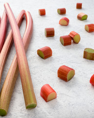 Fresh rhubarb and cut pieces of rhubarb on textured white marbled background. Shallow depth of field.
